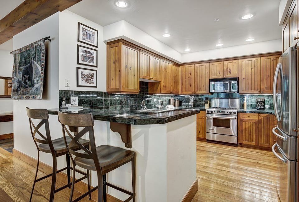 Kitchen with dark wood cabinetry, stainless steel appliances, granite countertops, bar seating, and under-cabinet lighting.