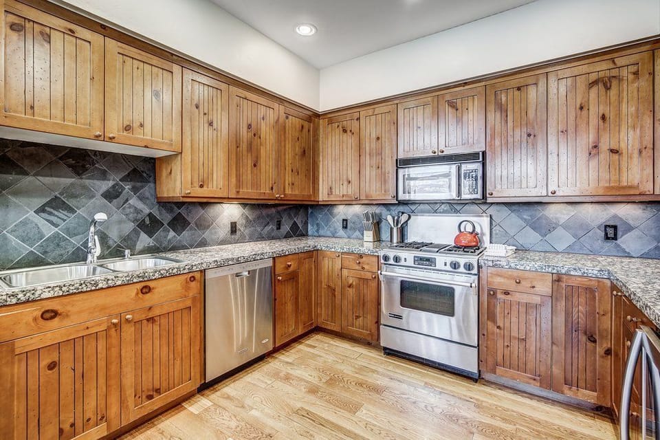 Fully equipped kitchen with granite countertops, stainless steel appliances, slate tile backsplash, and ample wood cabinetry.