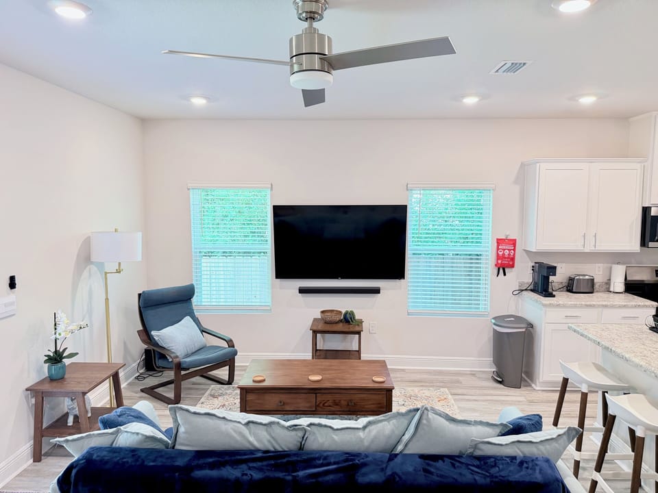 Bright open living room with large TV, stylish seating, and kitchen bar