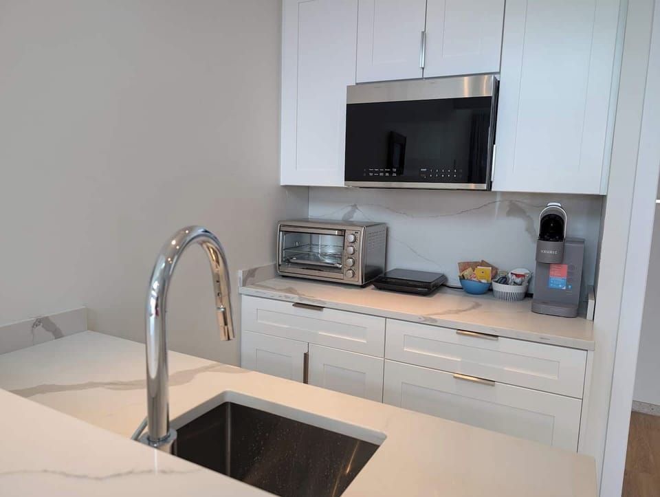Sleek kitchenette with quartz counters, stainless sink, induction cooktop, microwave, toaster oven, coffee maker, and access to a private BBQ for easy indoor-outdoor meals.