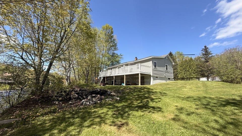 Spacious backyard with a large wraparound deck, open lawn, and peaceful wooded surroundings.