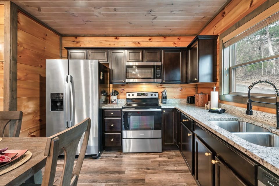 Fully equipped kitchen features stainless steel appliances, dark wood cabinetry, and sleek granite-style countertops.