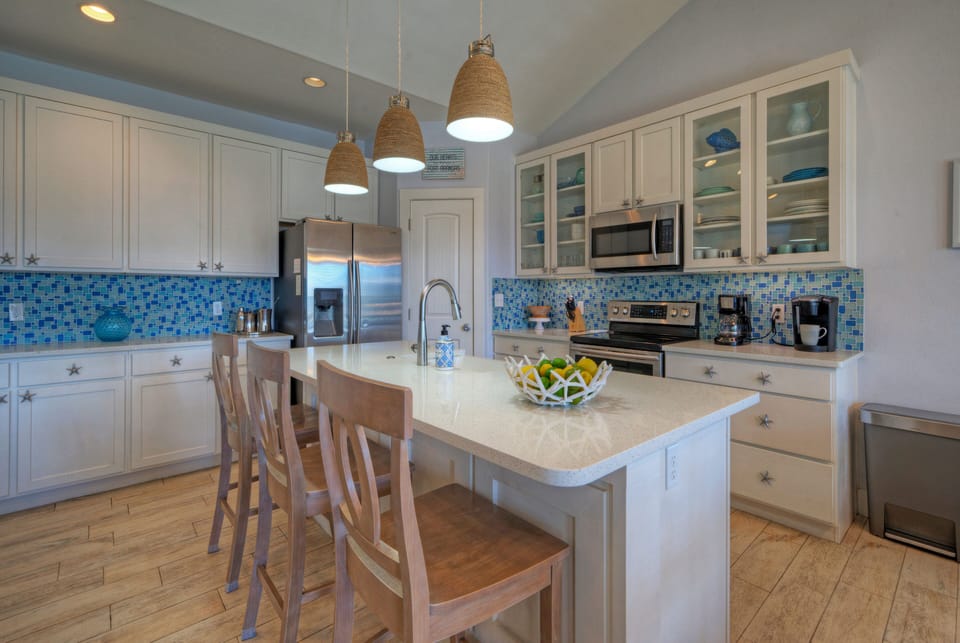 Bright kitchen featuring white cabinetry, a large island with seating, and blue tile backsplash.