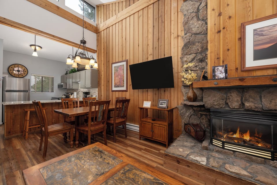 Cozy up by your stone fireplace while enjoying meals at the rustic dining table, with modern kitchen convenience nearby.
