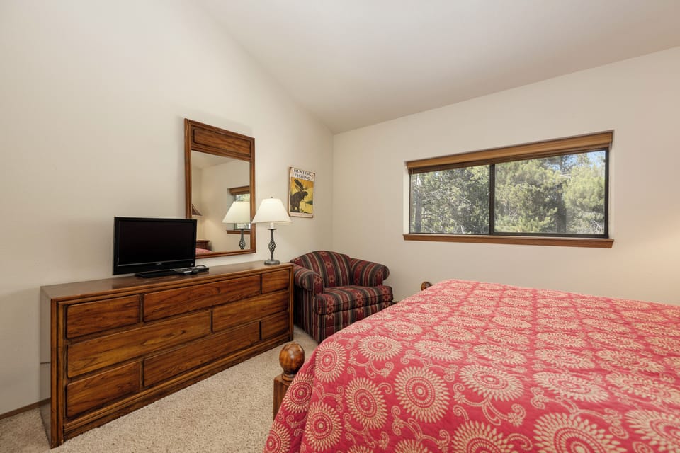 Relax in your cozy bedroom with warm wood furnishings, comfortable seating, and peaceful tree views through your private window.