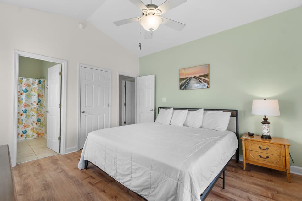 Unwind in your peaceful bedroom with soft linens, gentle ceiling fan, and calming green accent wall that creates a serene retreat.