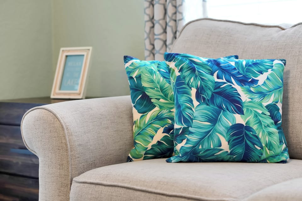 Sink into this cozy armchair with tropical pillows and let your vacation mindset bloom in this thoughtfully designed living space.
