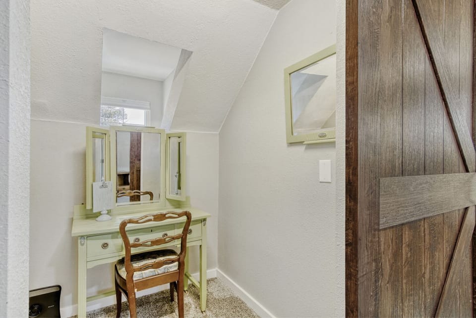 Your private vanity nook tucked behind the barn door in the primary bedroom offers a perfect spot for morning routines, featuring charming vintage-style furnishings and rustic barn door details.