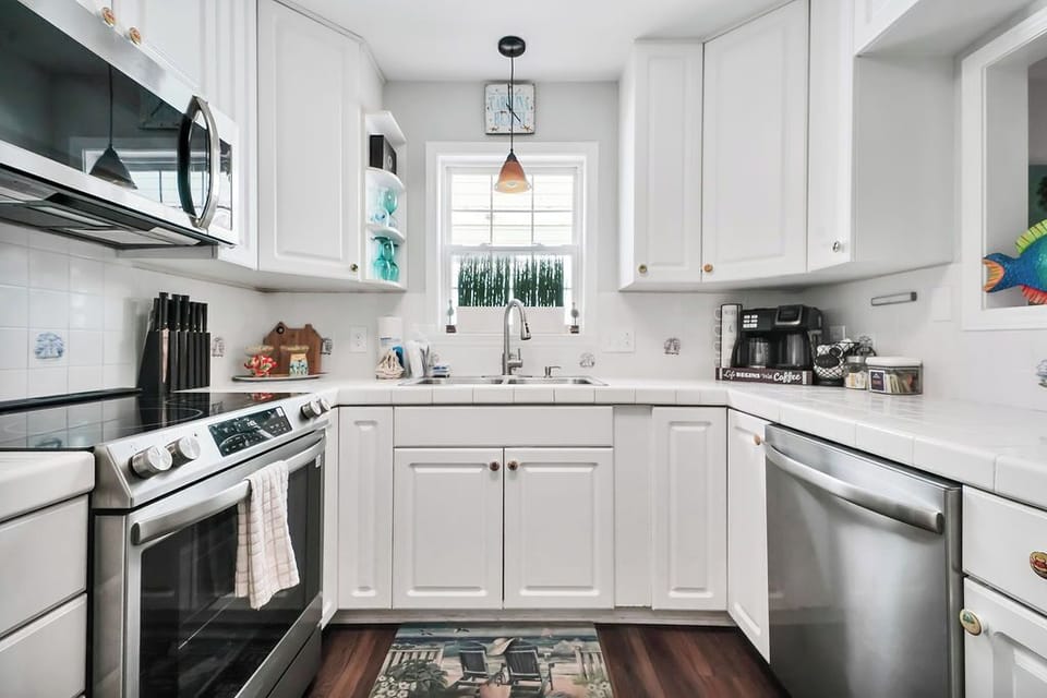 Your bright, fully-equipped kitchen invites you to cook with crisp white cabinets, stainless steel appliances, and morning light through the window.