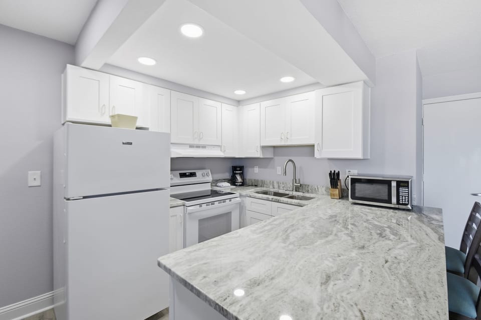 The kitchen beckons culinary creativity, boasting pristine white cabinetry, gleaming granite countertops, and essential appliances, all set against a tranquil backdrop.