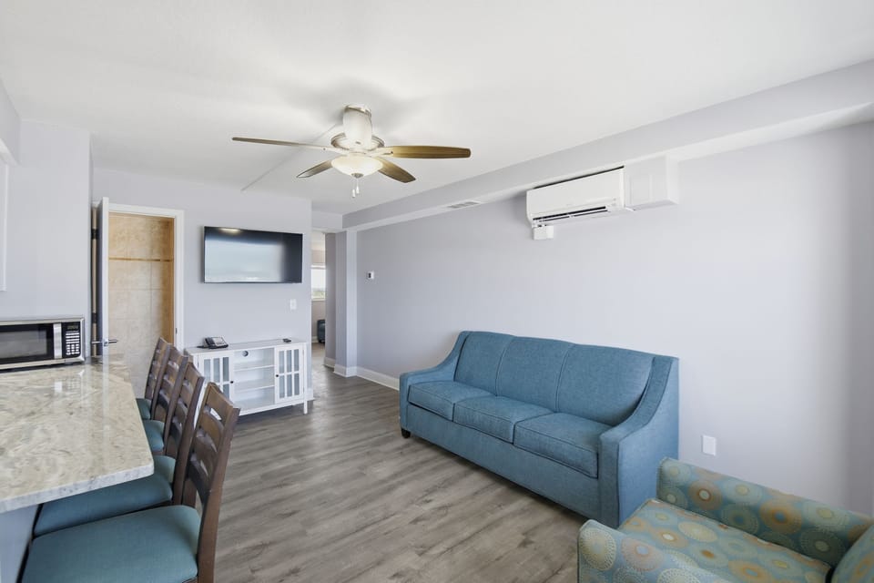 Relax in the cozy living area, furnished with a stylish sofa and plush chairs, providing the perfect space to unwind after beach adventures, all under the gentle hum of the ceiling fan.