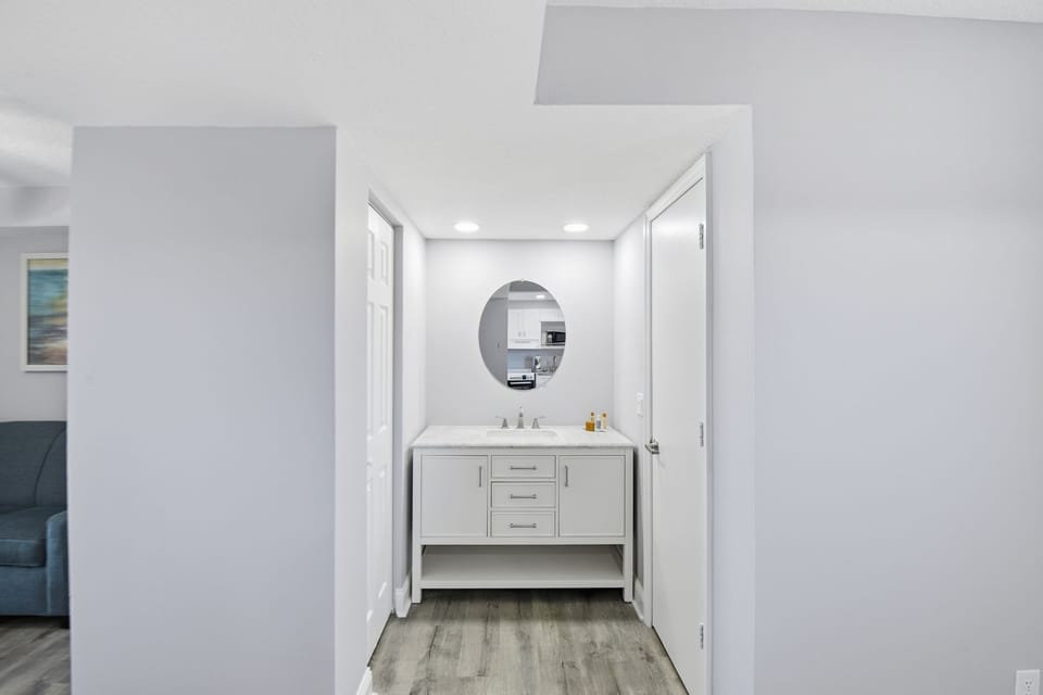 The sleek bathroom area includes a chic vanity with dual sinks, elegant lighting, and a spacious layout that seamlessly transitions to the rest of the suite, emphasizing modern design.
