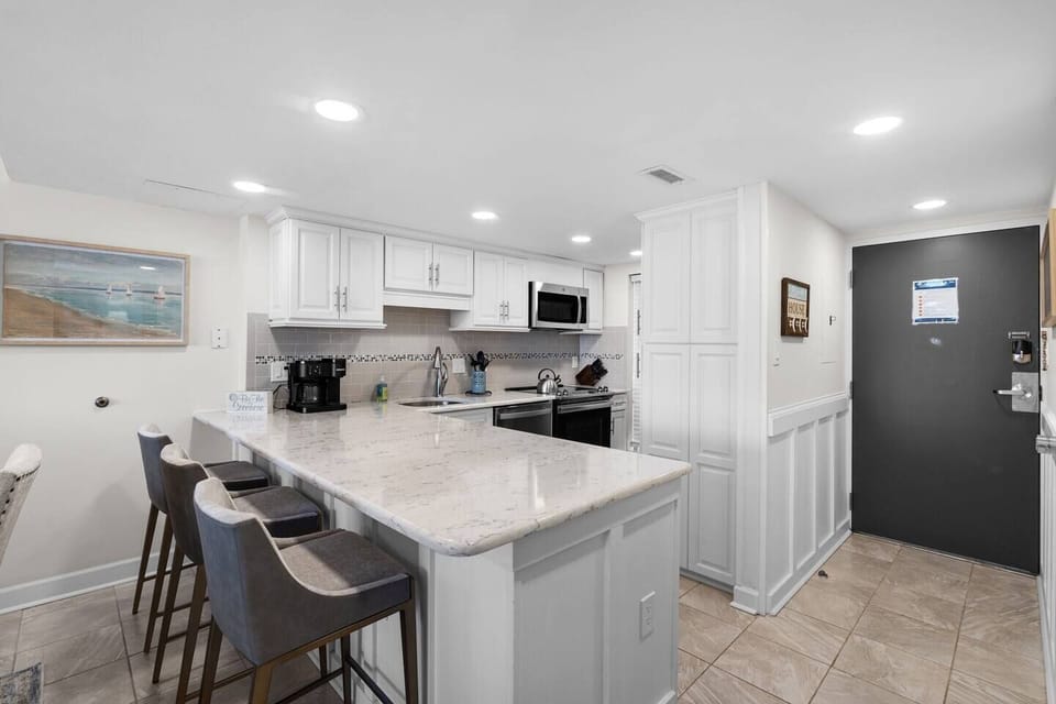 Modern coastal kitchen featuring white cabinetry, stainless appliances, and island seating.