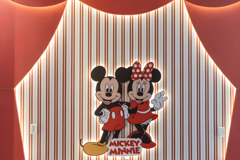 Experience a playful atmosphere with vibrant striped walls and soft lighting, highlighted by a charming Mickey and Minnie display that invites guests of all ages to relax and enjoy their stay in this whimsical setting.