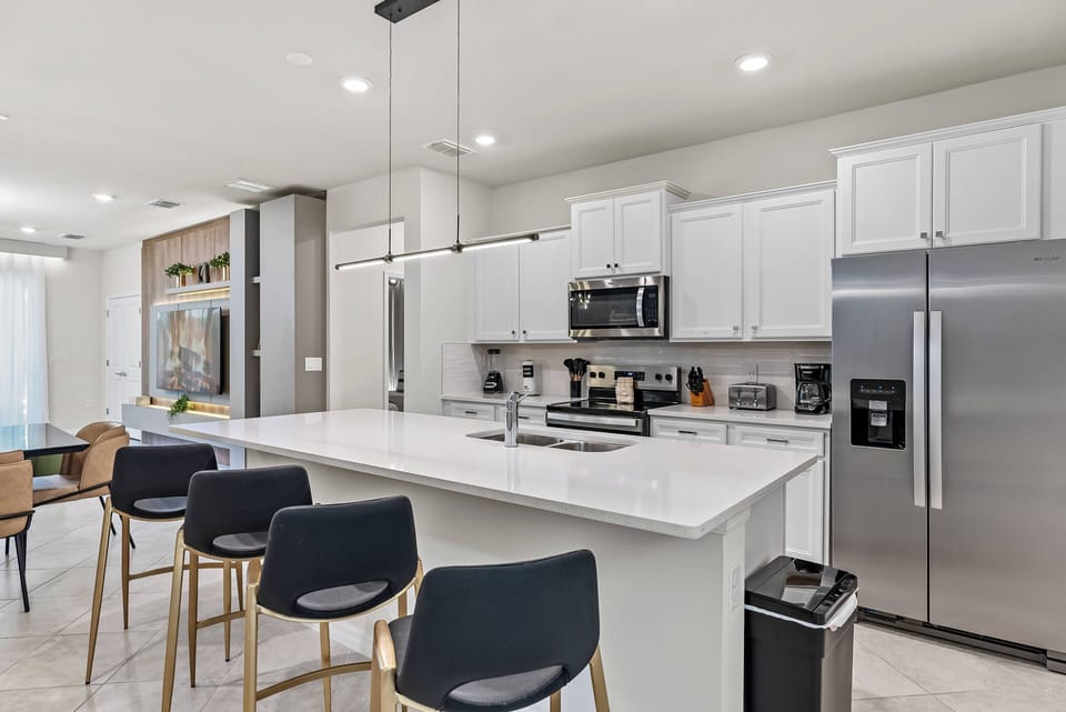 Experience a delightful stay in this stylish kitchen featuring sleek white cabinets, a spacious island for casual seating, stainless steel appliances, and polished countertops, all complemented by inviting natural light.