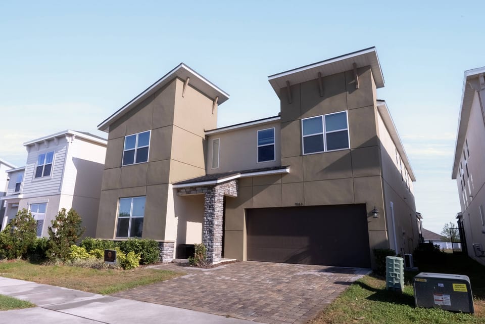 Experience a charming exterior with textured earth tones and sleek lines, where large windows fill the interior with natural light. The elegant stone entrance offers easy access to the landscaped yard and various amenities.
