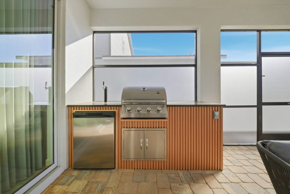 Step outside to your stylish outdoor kitchen with a sleek stainless steel grill and warm wooden countertop. Large windows fill the space with natural light, making it perfect for al fresco dining and entertaining.