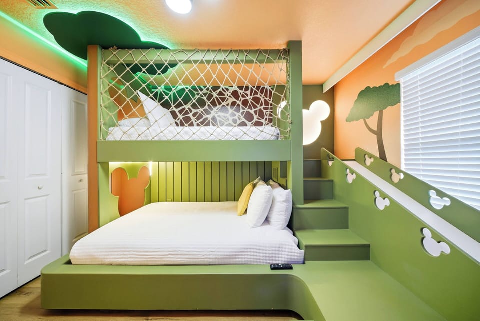 This playful bedroom boasts a unique lofted bed with a cozy lower level, surrounded by vibrant green and orange walls with whimsical tree motifs. Soft bedding and fun textures make it a welcoming space perfect for relaxation.