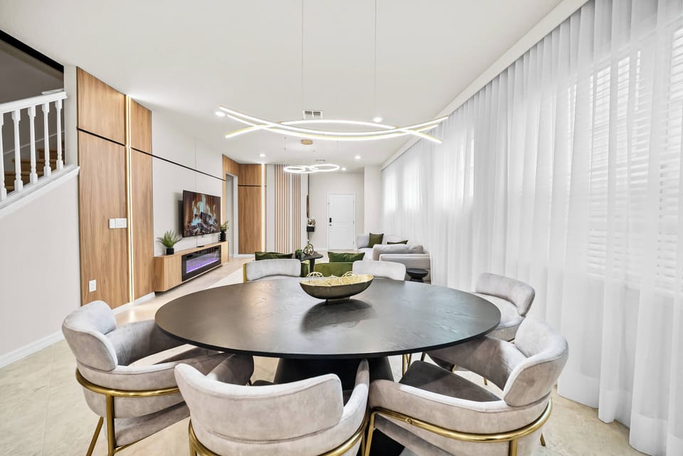 Gather around the stylish black dining table, with inviting light-colored chairs. Natural light filters through sheer curtains, enhancing the modern décor and creating a warm, welcoming space for meals and conversations.