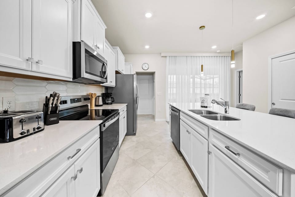 This stylish kitchen boasts sleek white cabinetry and a spacious countertop perfect for cooking and chatting. Modern appliances and abundant natural light create a bright, functional space for all your culinary adventures.