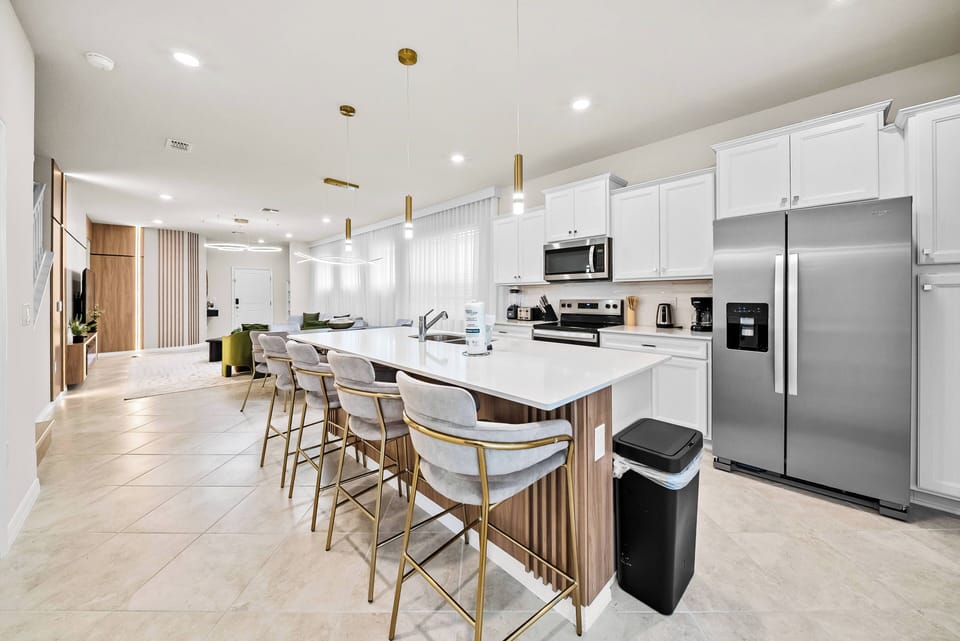 This modern kitchen boasts a spacious island with stylish bar seating, perfect for casual meals or morning coffee. The bright white cabinetry harmonizes with warm wood accents, creating an inviting and welcoming atmosphere.