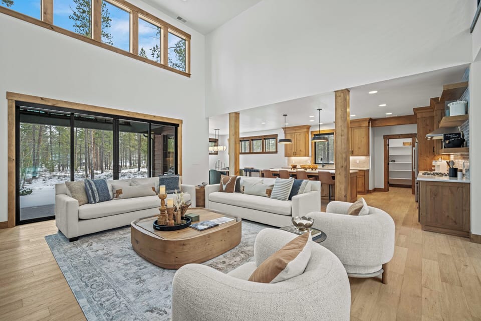 Unwind in this stunning open-concept living space where soaring ceilings and expansive windows frame winter forest views, creating your perfect mountain retreat.