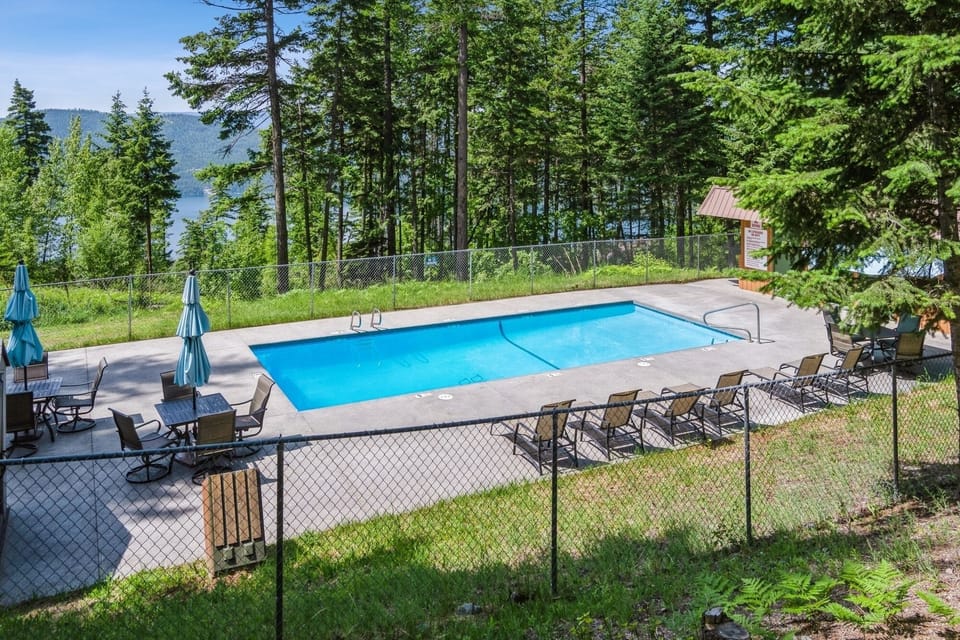 Swimming pool nestled among towering pines with mountain lake views beyond the forest.