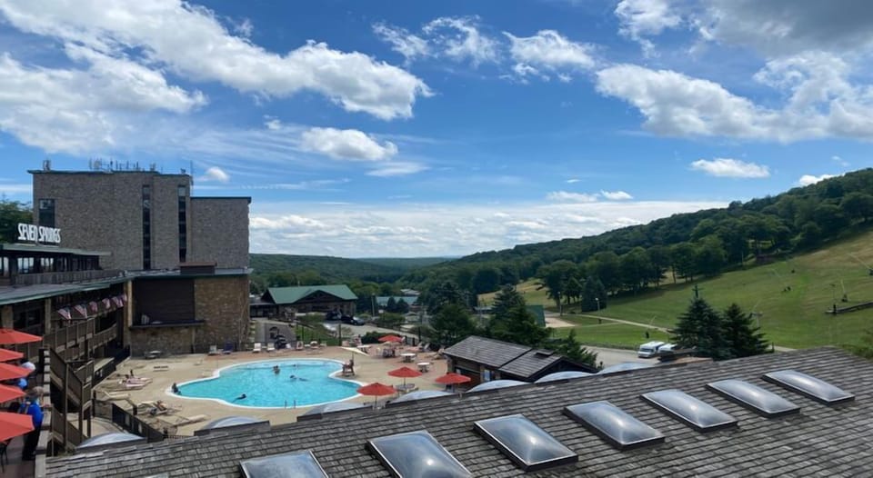 A panoramic view reveals the vibrant blue pool nestled against rolling hills and a bright sky.