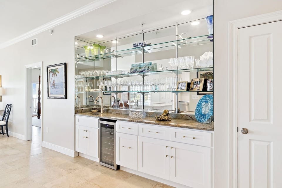Your elegant wet bar awaits with gleaming glass shelving, wine cooler, and granite counters perfect for entertaining guests.