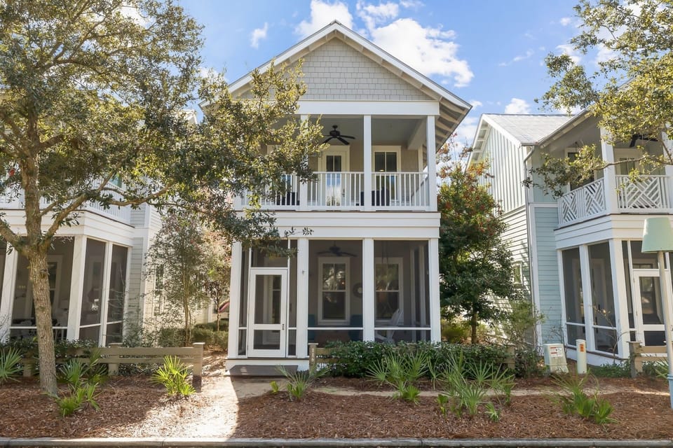 Charming coastal cottage with classic architecture, front porch, and mature oak trees in a peaceful residential setting.