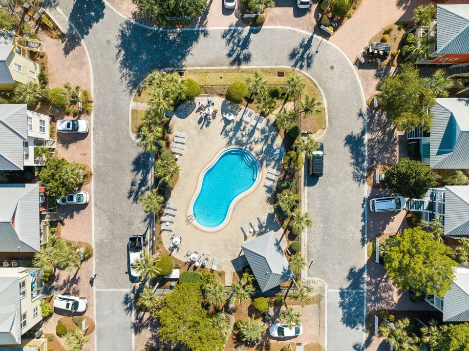 Aerial view of a resort community featuring a central swimming pool surrounded by tropical landscaping and vacation rental homes.
