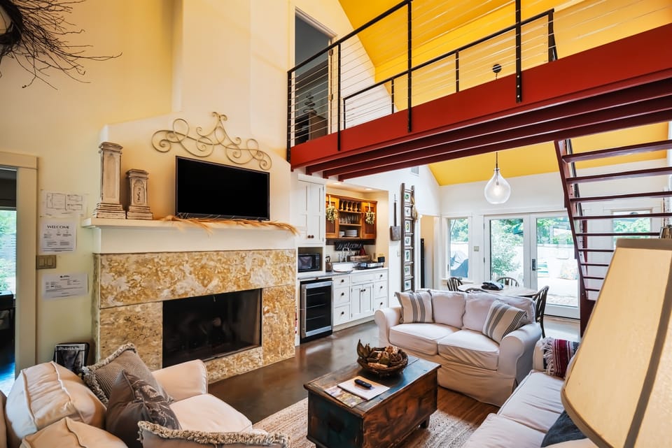 Bright open-concept living space with loft overlook, stone fireplace, and inviting seating area.