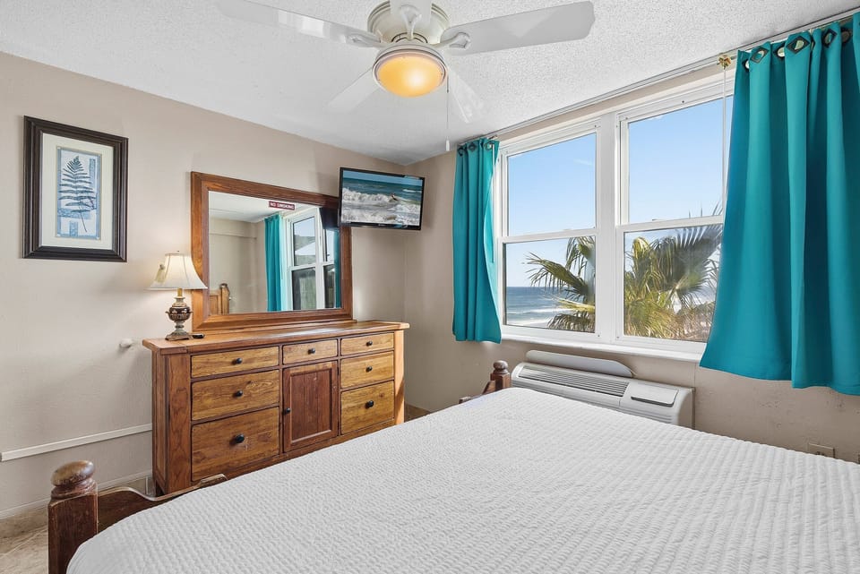 Wake up to beautiful ocean views in this cozy coastal bedroom featuring a plush bed and bright windows overlooking the shoreline. This beach stay vacation rental offers the perfect blend of comfort and seaside charm.