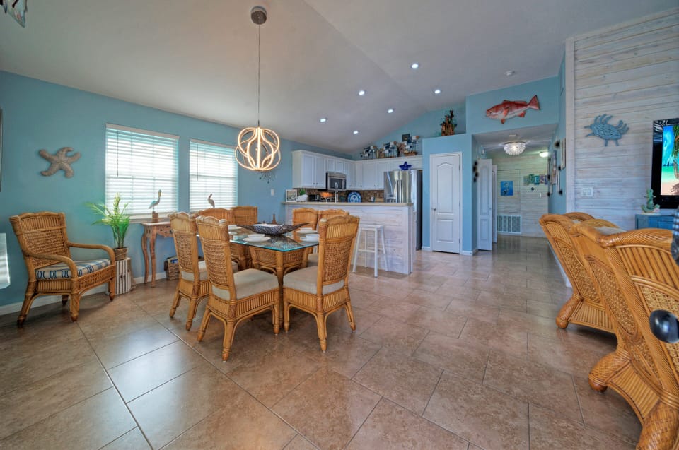 Dining area with a glass-top table, wicker chairs, and a decorative chandelier.