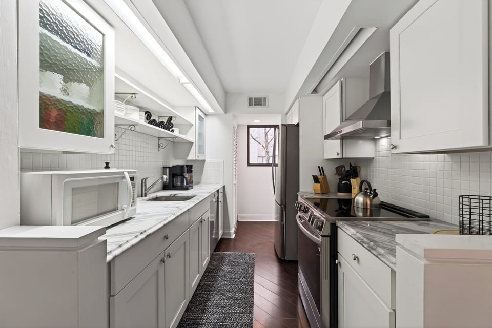 Sleek galley kitchen with white cabinetry, stainless steel appliances, and elegant marble-style countertops.