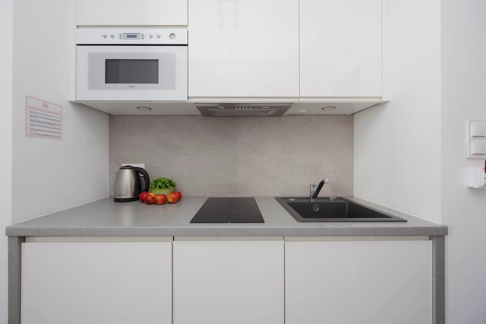 A detailed shot of the kitchen workspace featuring a grey countertop with a kettle and fresh fruit. White minimalist cabinets and a grey tiled backsplash contribute to the clean, contemporary design.