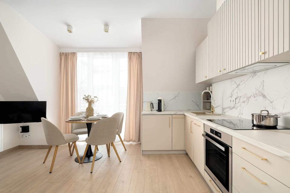 Another kitchen view showing white cabinets, countertops, and a dining table nearby. The space is bright and well-organized. Natural light enhances the clean design.