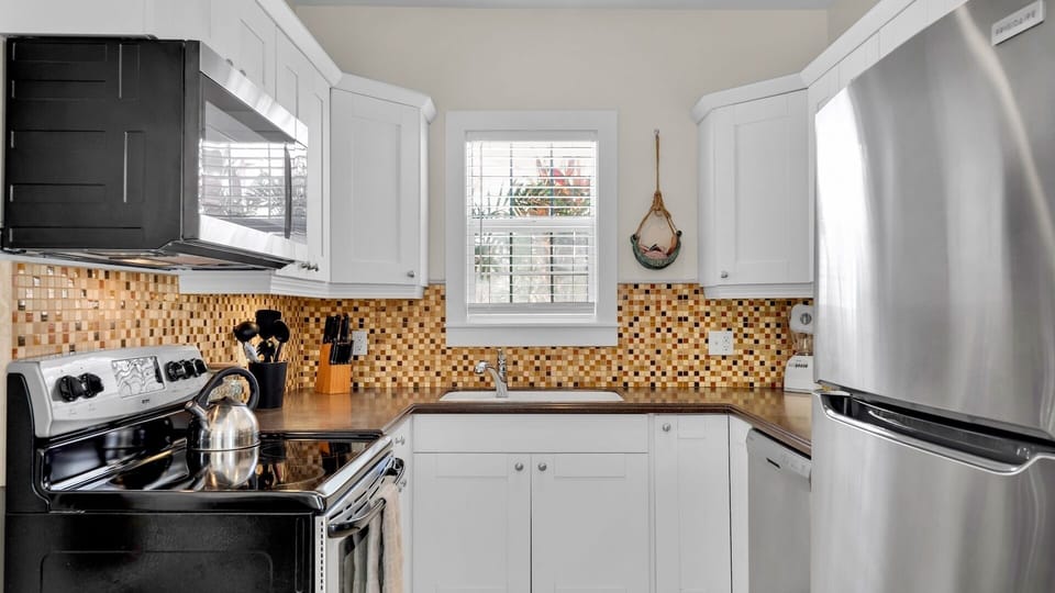 Your modern kitchen features gleaming appliances and warm mosaic tile backsplash, perfect for preparing meals with natural light streaming through the window.