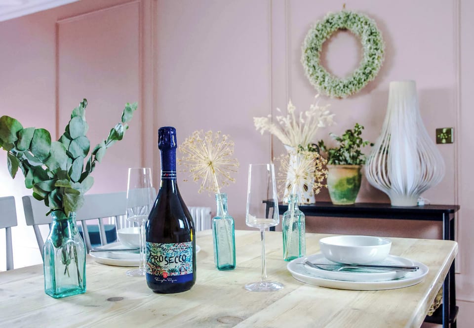 A stylish countryside retreat with a modern kitchen, cream cabinetry, built‑in oven, and fridge. A wooden dining table with soft chairs sits under a pendant light, creating a warm, inviting space for up to 7 guests.