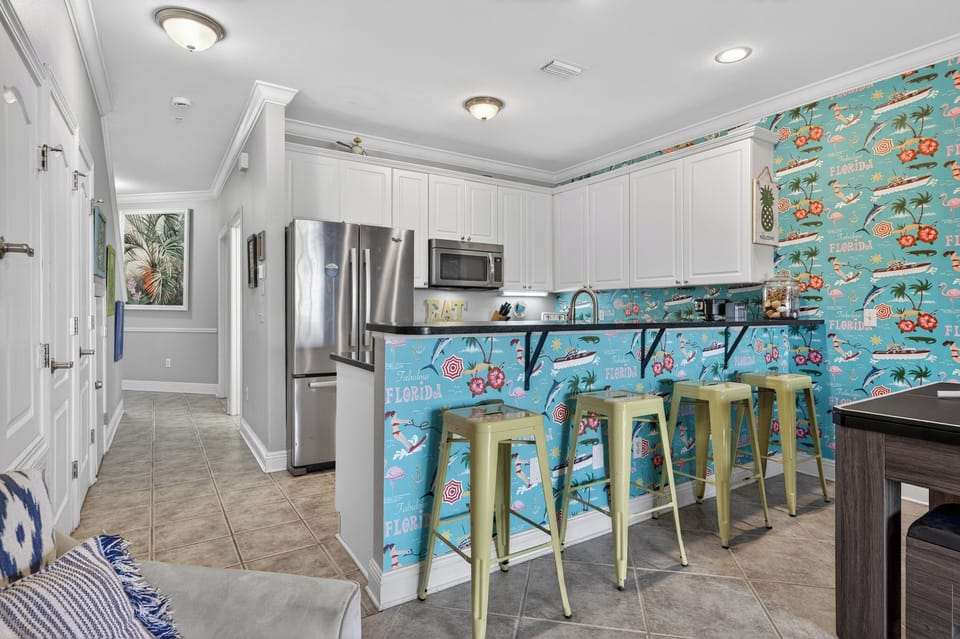 Colorful bar area with seating for 4. Fully stocked kitchen in distance.