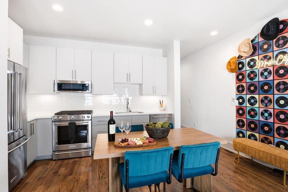 The kitchen opens straight to the dining table and living room, fully stocked for group cooking. Teal chairs and record art make every meal feel like part of the celebration