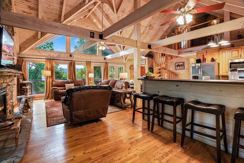 Rustic great room with vaulted ceilings, fireplace, and forest views