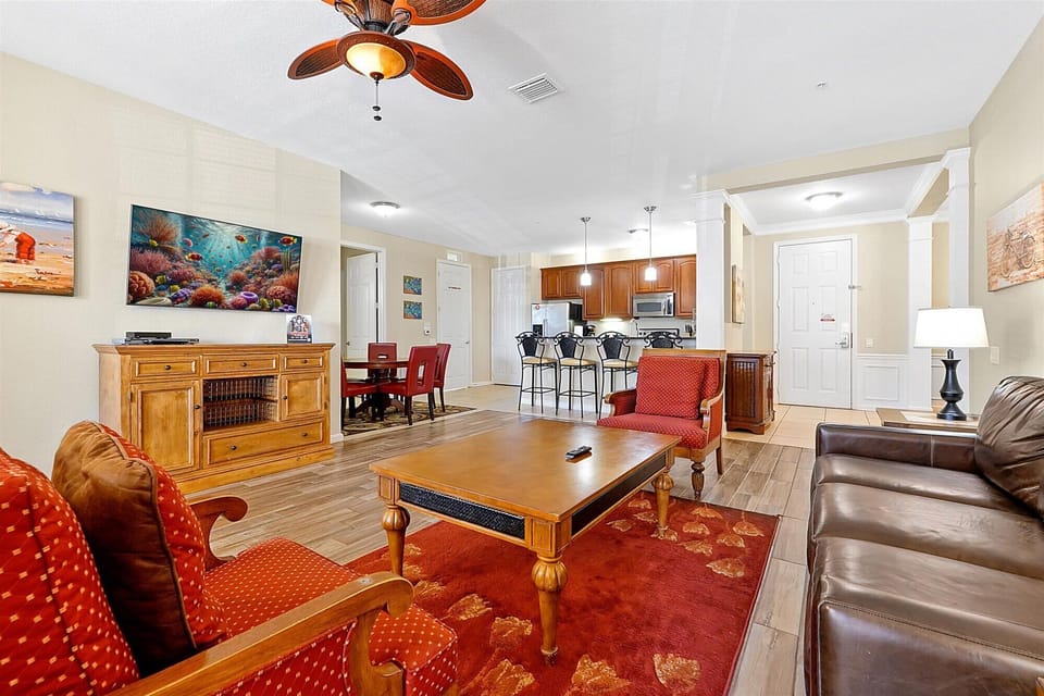 Relax in your open-concept living space featuring warm wood furnishings, leather seating, and vibrant coral artwork that creates a coastal ambiance.