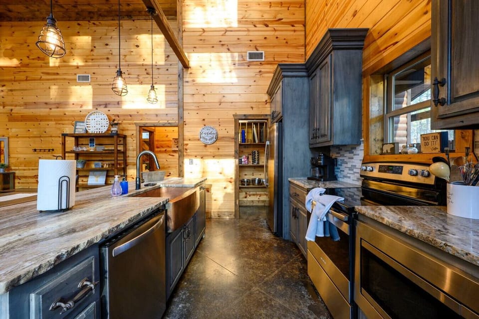 This stunning log cabin kitchen features custom dark cabinetry, stainless steel appliances, and soaring wood ceilings with pendant lighting.