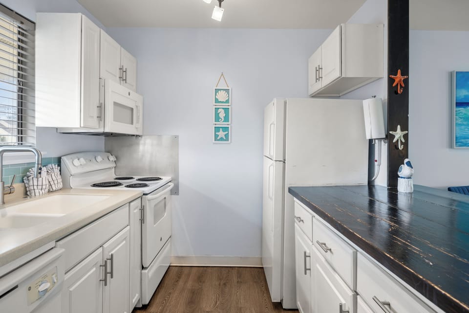 Your bright galley kitchen features white cabinets, full appliances, and coastal decor perfect for preparing beach day snacks.