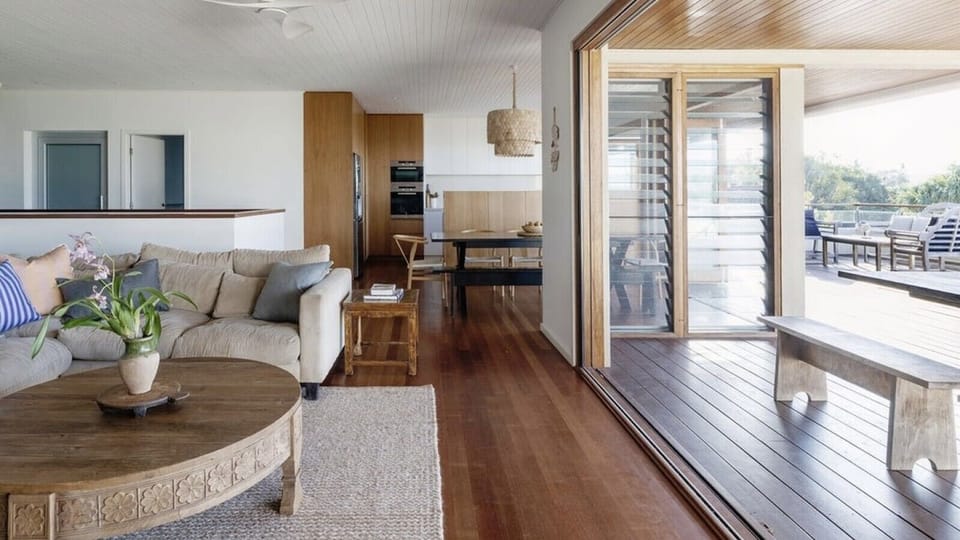 Relaxed lounge flowing through to the kitchen and out to the deck, filled with natural coastal light.