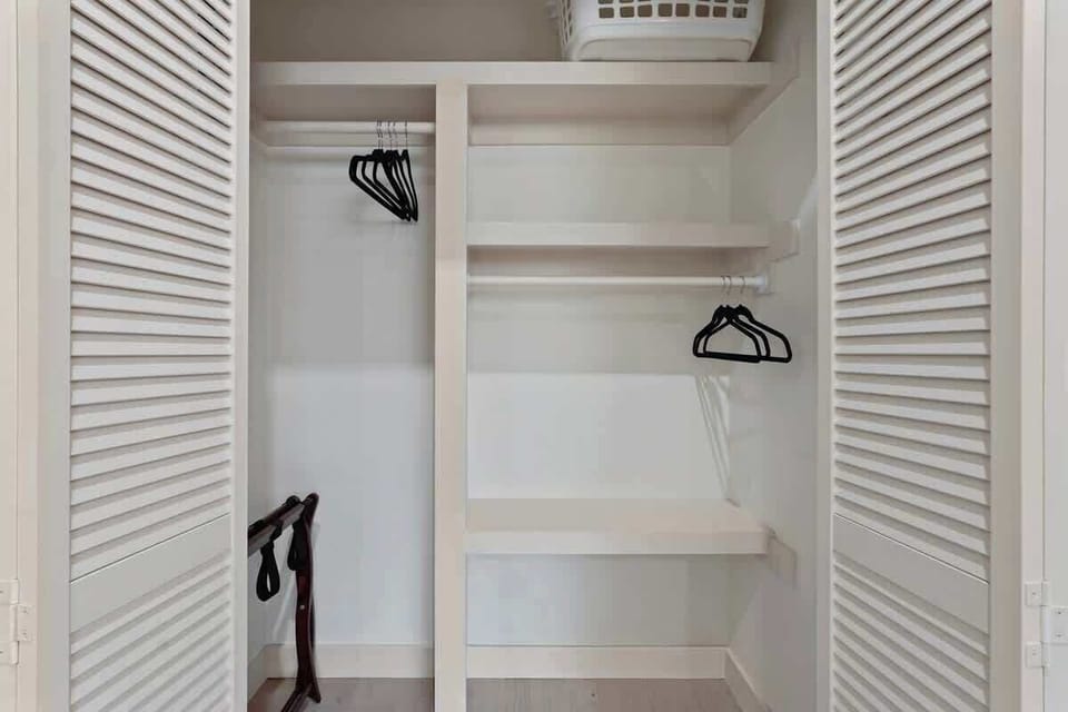 Spacious closet with built-in organization. Louvered doors open to reveal hanging space, shelving, luggage rack, and laundry basket. Plenty of storage for extended stays.