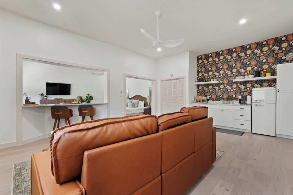 Designer kitchenette with bold floral wallpaper. Statement wall featuring colorful botanical print, retro-style white refrigerator, marble countertops, open shelving, and breakfast bar seating.