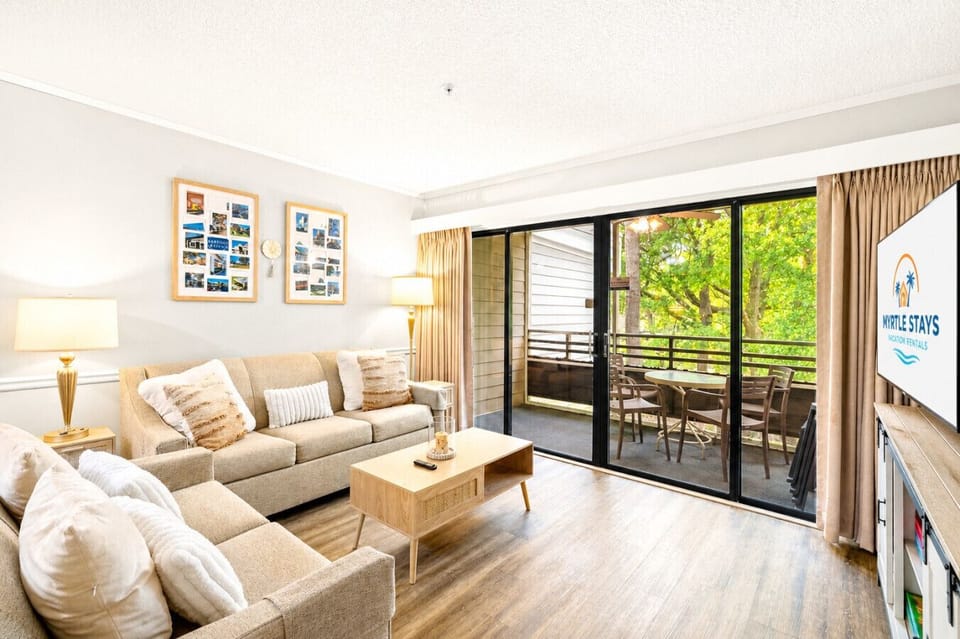 Another bright view of the peaceful living room featuring cozy seating, HD Smart TV, private balcony access, and beautiful natural light throughout.