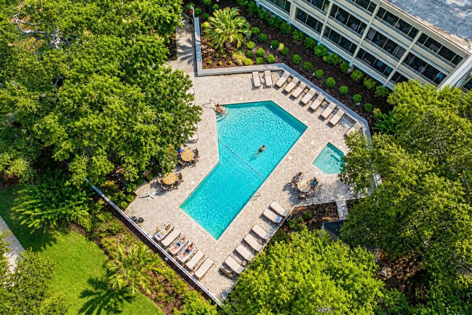 Bright aerial view of Ocean Creek Lodge pool featuring sparkling water, sun loungers, poolside chairs, and sunny resort-style relaxation.
